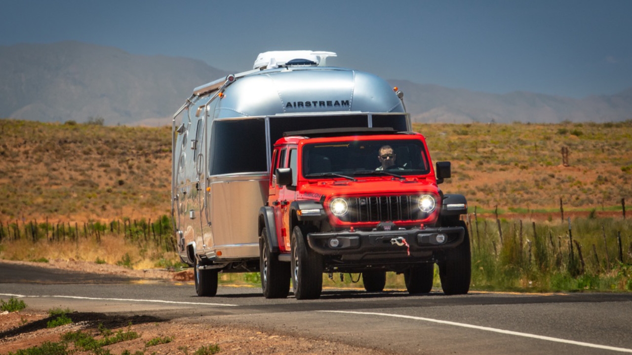 vue latérale avant d'un Jeep Wrangler 2025 remorquant une roulotte sur une route dans le désert